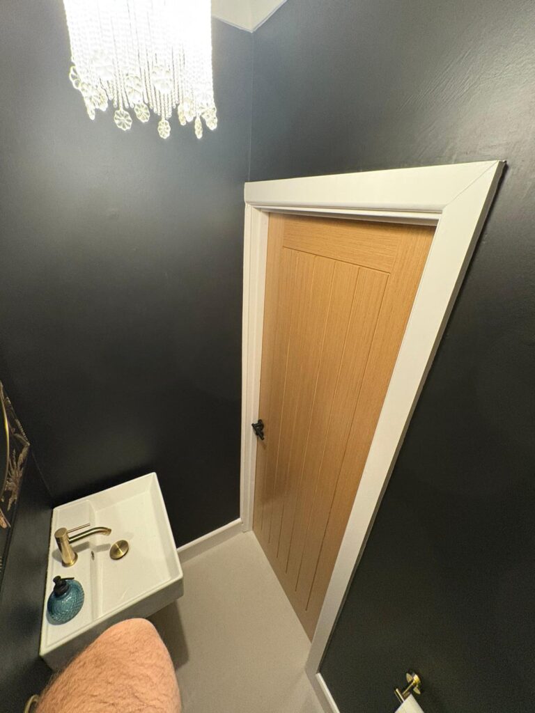 Photo of a white sink, small crystal chandelier and a brown wooden door.